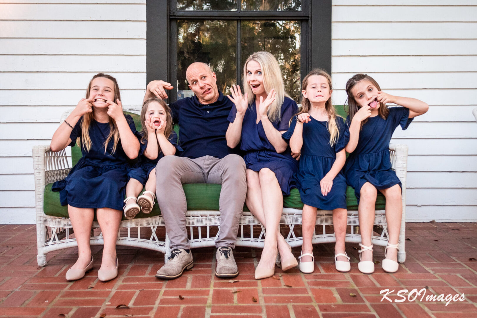 A family wearing navy blue clothes and doing silly poses