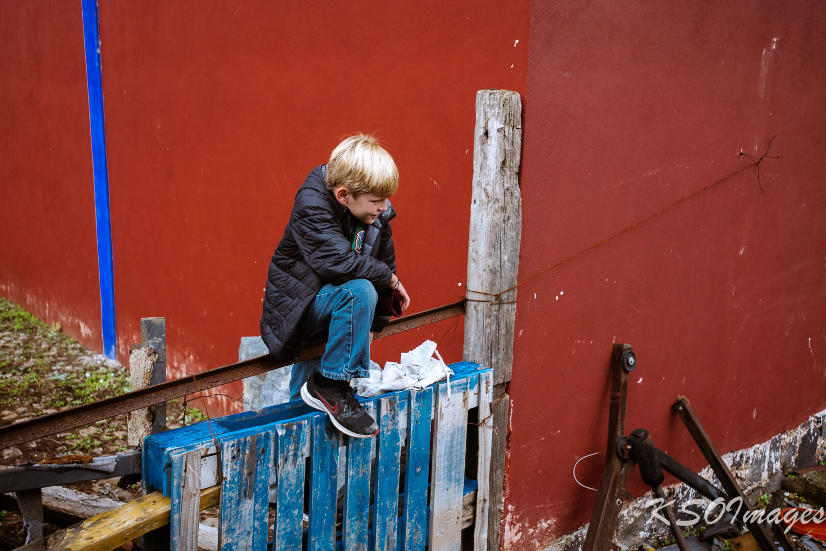 A Boy Sitting on a Blue Color Fence