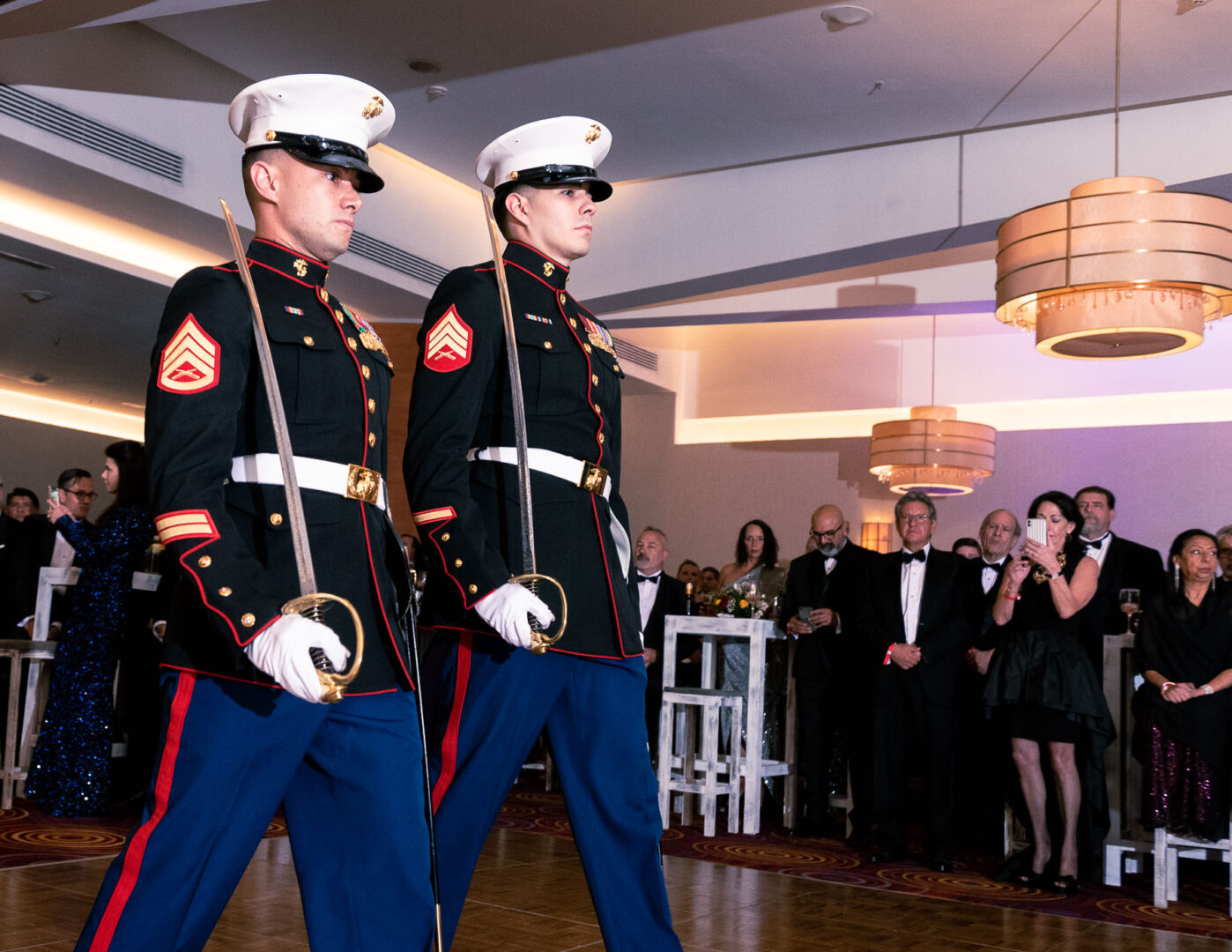 Two men in uniform holding a sword in one arm and walking